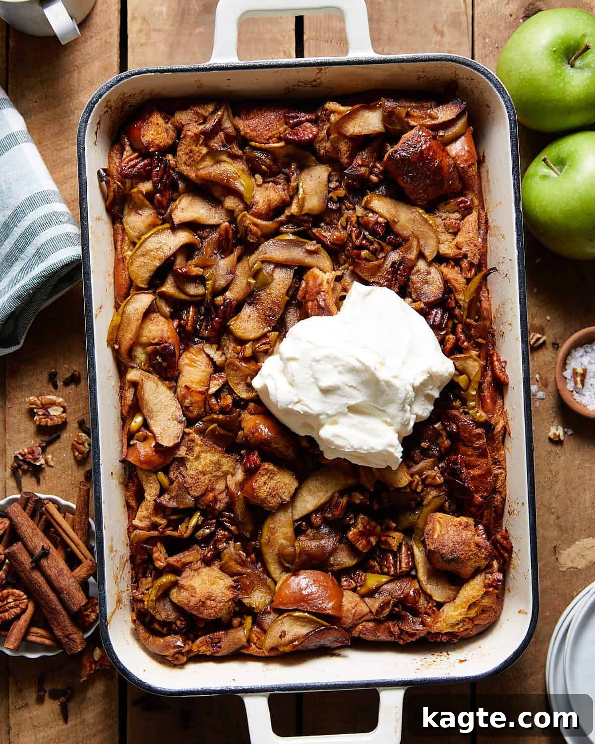 Warm Apple Bread Pudding in a white casserole dish, generously topped with homemade whipped cream, ready to be served.