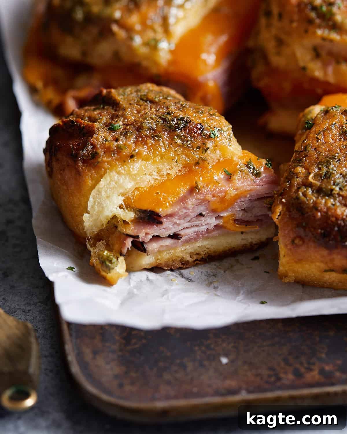 Irresistible King's Hawaiian Ham and Cheese Sliders 2 Golden brown King's Hawaiian ham and cheese sliders on parchment paper, fresh from the oven, ready to be served.