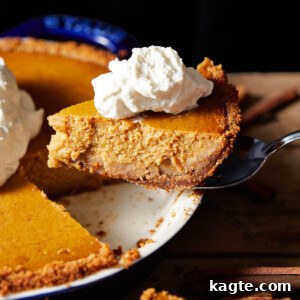 A freshly baked pumpkin pie with graham cracker crust, still in its blue pie dish, showing a perfectly set filling and golden crust. A warm, inviting image of the complete dessert.