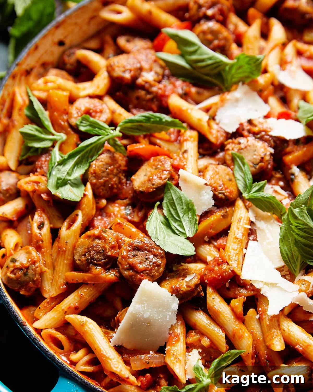 Quick Weeknight Sausage and Pepper Pasta 6 A close-up shot of Italian sausage pasta and peppers, garnished with fresh basil, served in a rustic blue pot.