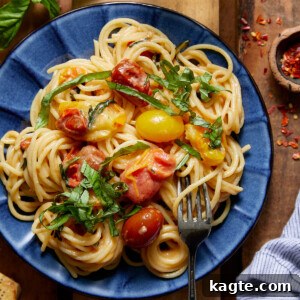 A close-up of vibrant basil pasta with cherry tomatoes on a blue plate, ready to be served, garnished with fresh basil.