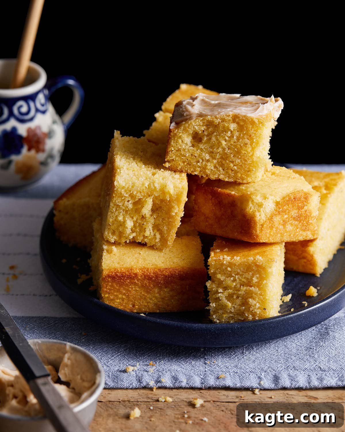 A stack of golden brown cornbread squares, perfectly baked, on a white plate, ready to be served.