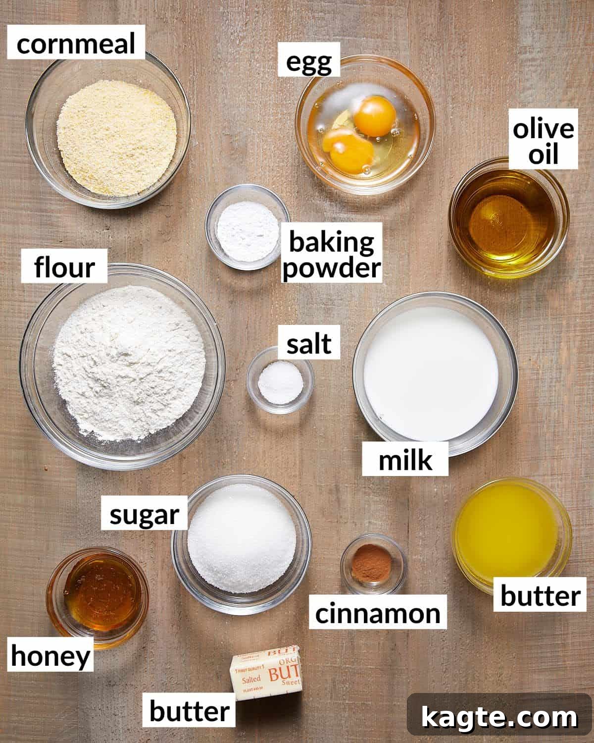 A collection of cornbread ingredients displayed in glass bowls, including cornmeal, flour, milk, sugar, butter, and eggs.