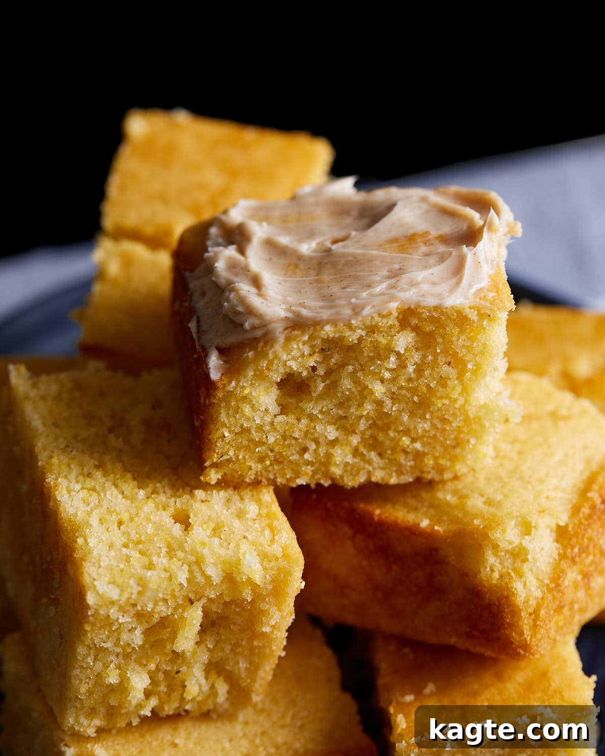 A perfectly baked slice of cornbread with a generous dollop of whipped honey cinnamon butter melting on top, on a white plate.