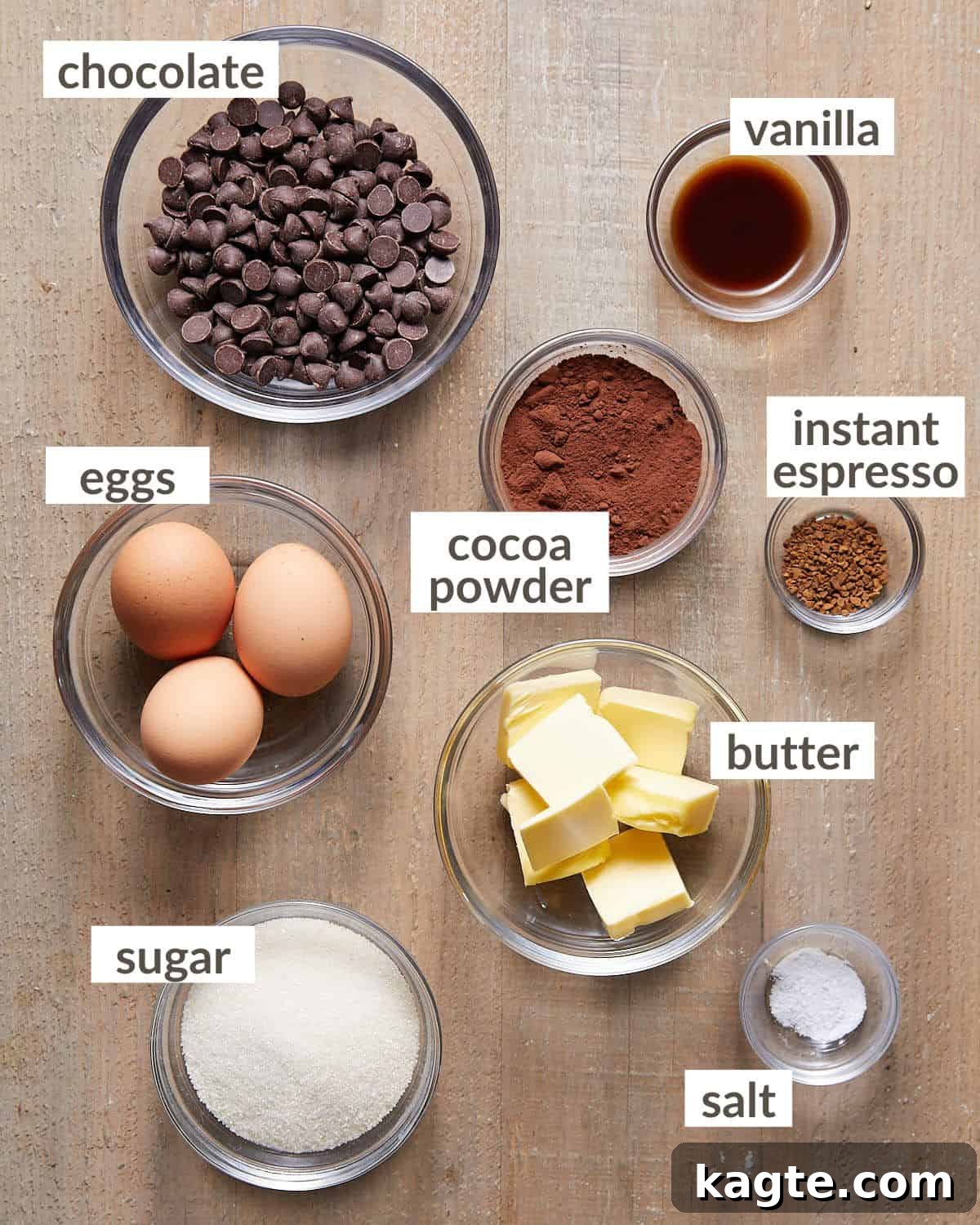 Overhead image of all necessary ingredients laid out for making mini flourless chocolate cakes, including chocolate, eggs, sugar, butter, and cocoa powder.