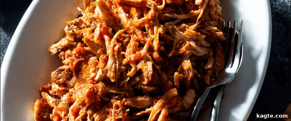 25 Hassle-Free Boneless Chicken Thigh Ideas 13 Tender oven-pulled chicken thighs, ready to be enjoyed, served in a white dish with a fork.