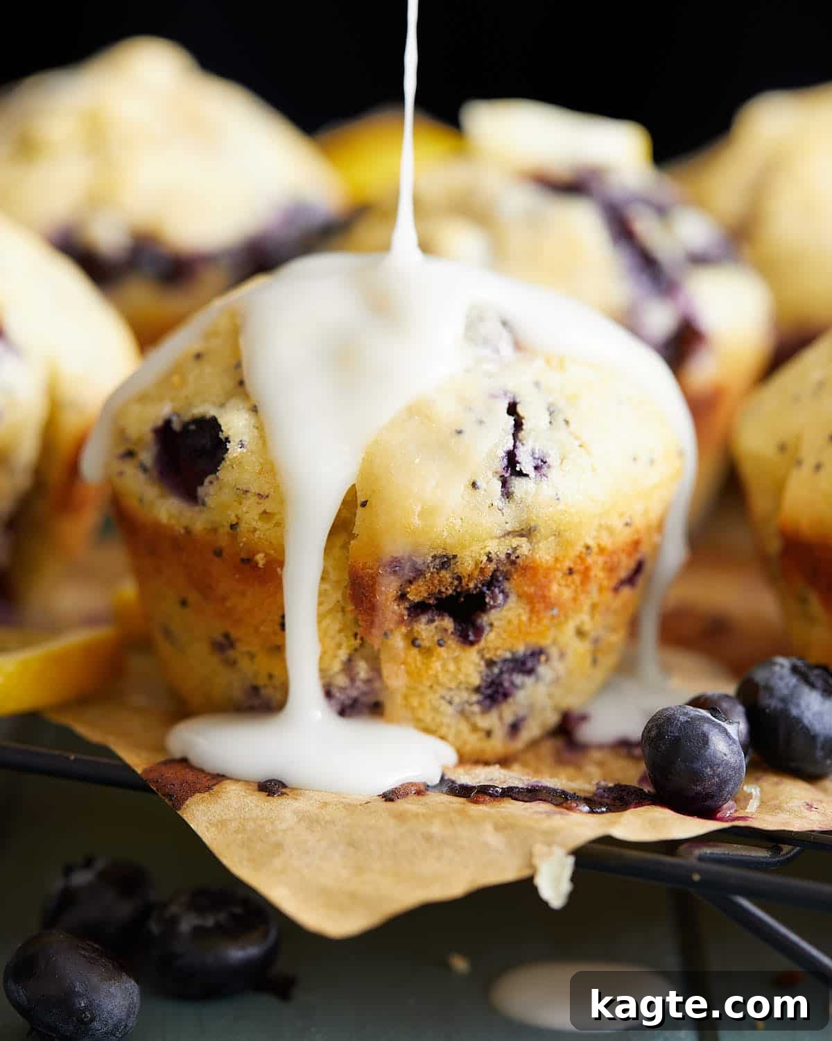Up close image of a single blueberry lemon poppy seed muffin, showcasing its tall dome and glistening lemon glaze.