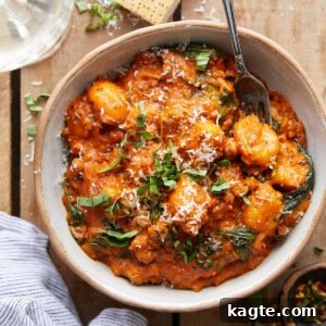 Close-up of creamy sausage gnocchi with vibrant spinach and rich tomato sauce in a pan, garnished with herbs.