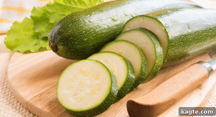 Three fresh green zucchinis lying on a surface, one sliced to show its inner texture.