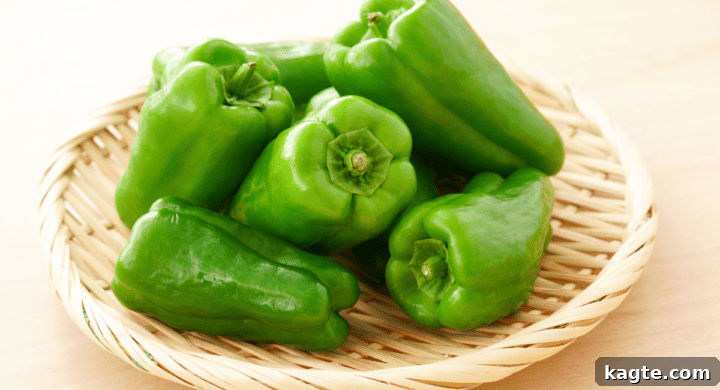 Three vibrant green bell peppers, one whole and two halved to reveal the seeds and inner structure.