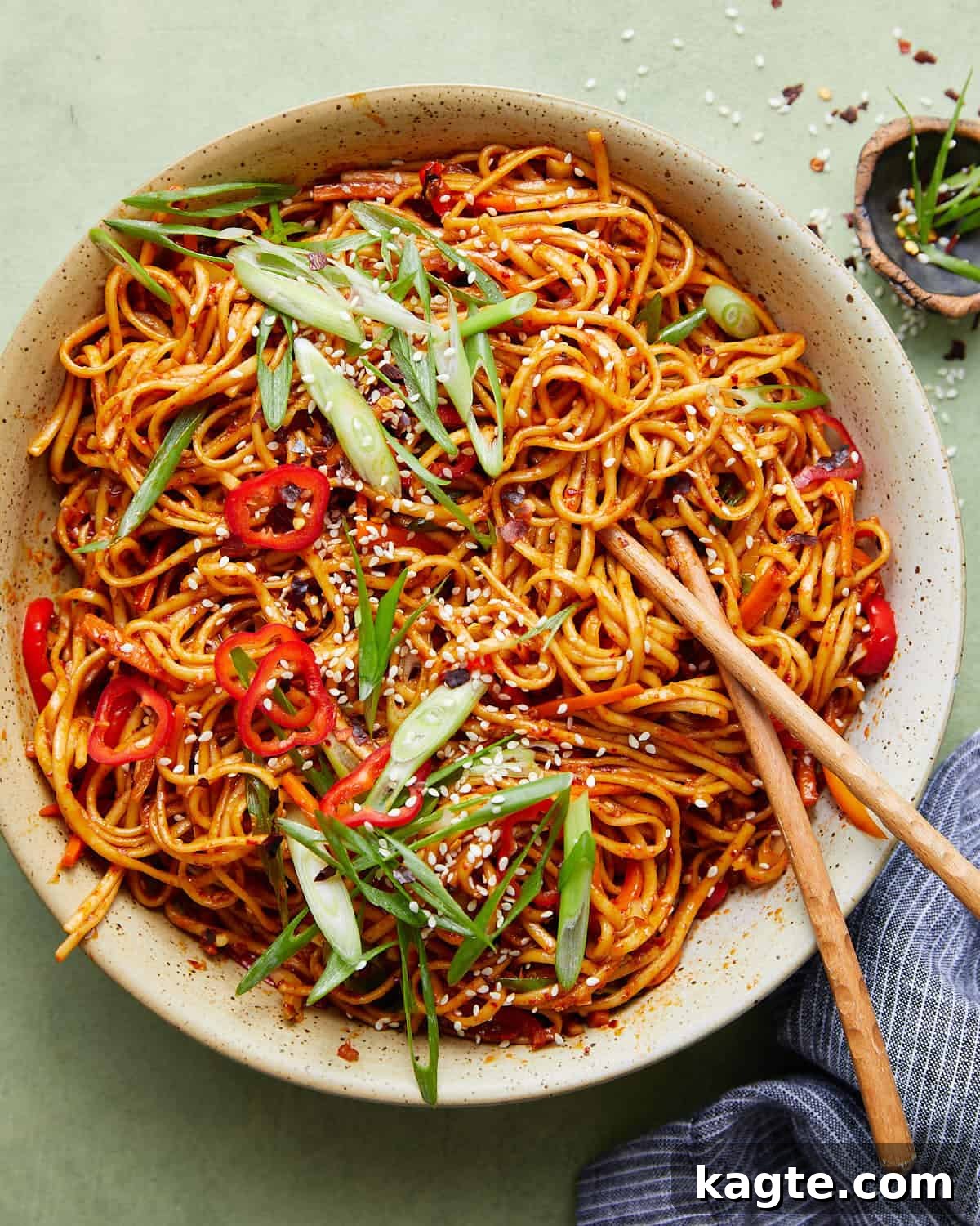 Sizzling Chili Garlic Noodles 2 A vibrant bowl of Chili Garlic Noodles garnished with green onions and sesame seeds.