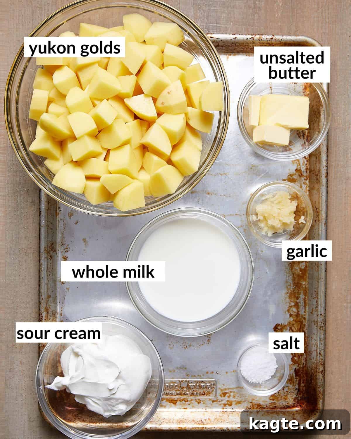 Velvety Yukon Gold Mash 3 Overhead image of ingredients needed for yukon gold mashed potatoes, including potatoes, butter, garlic, milk, sour cream, salt, and pepper.