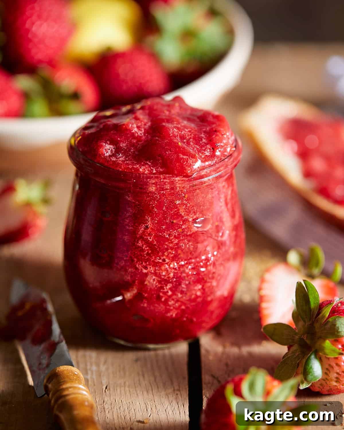 Up close image of delicious homemade strawberry preserves in a clear glass jar, showcasing the chunky fruit texture.