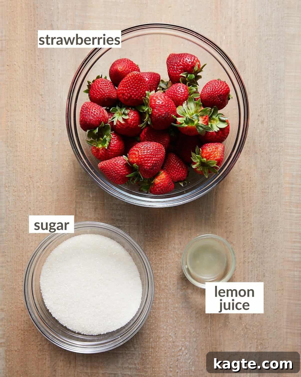 Overhead image of fresh strawberries, granulated sugar, and a lemon, the three ingredients needed for strawberry preserves.