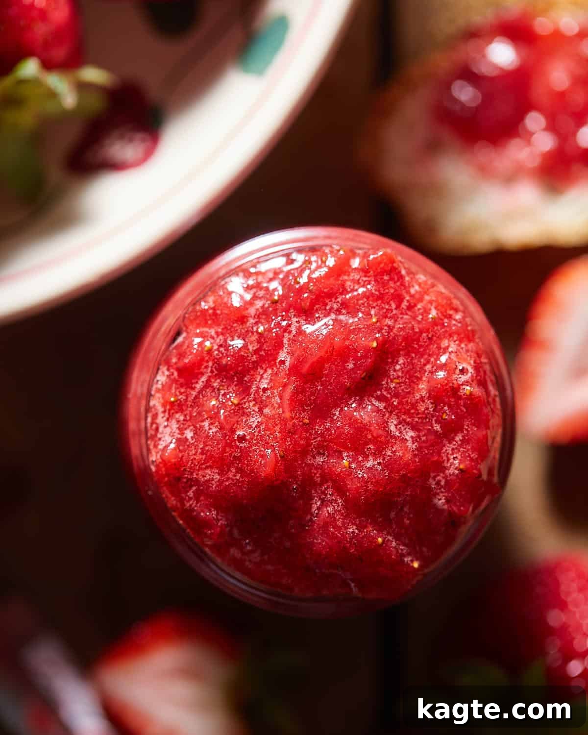 Overhead image of freshly made strawberry preserves in a glass jar, highlighting the whole and chunky fruit pieces.