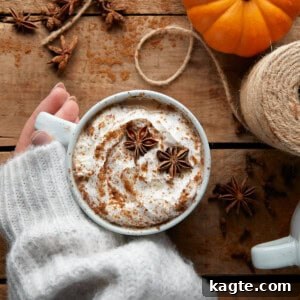 A pumpkin spice chai latte in a clear glass mug, topped with whipped cream and a sprinkle of spice.