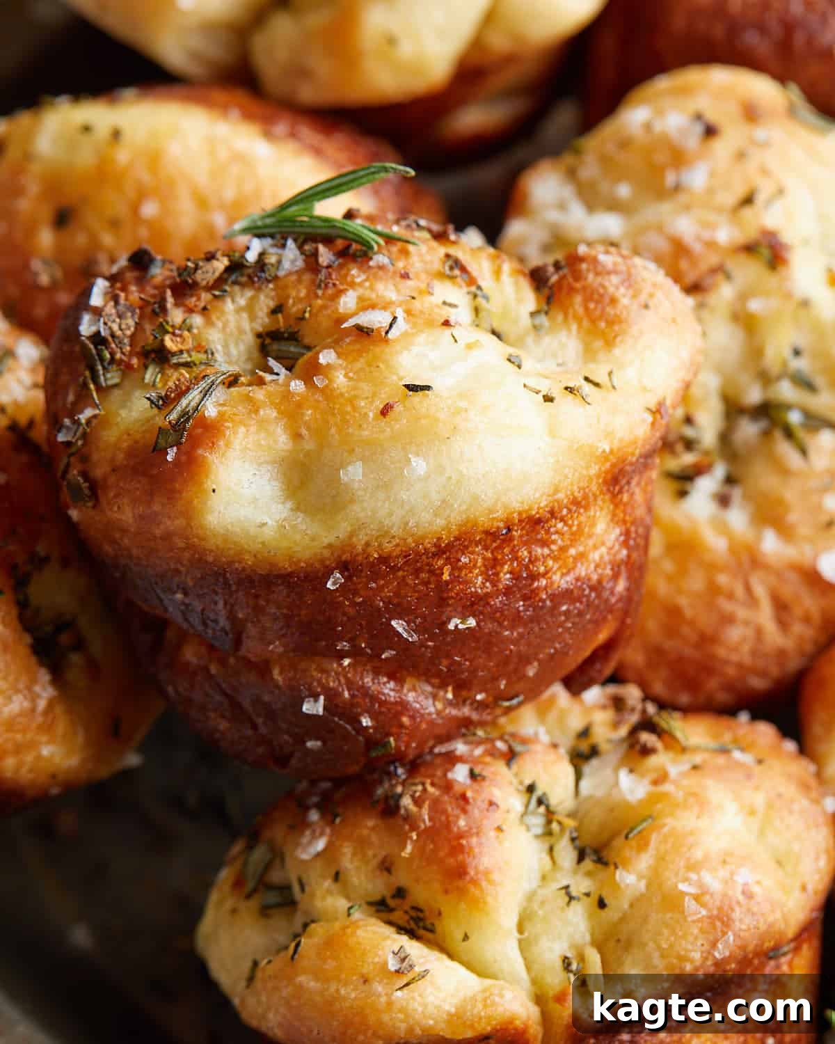 Aromatic Garlic Rosemary Focaccia Bites 6 Close-up image of a single focaccia muffin, showcasing its golden crust, dimples, and garnishes of rosemary and flaky salt.