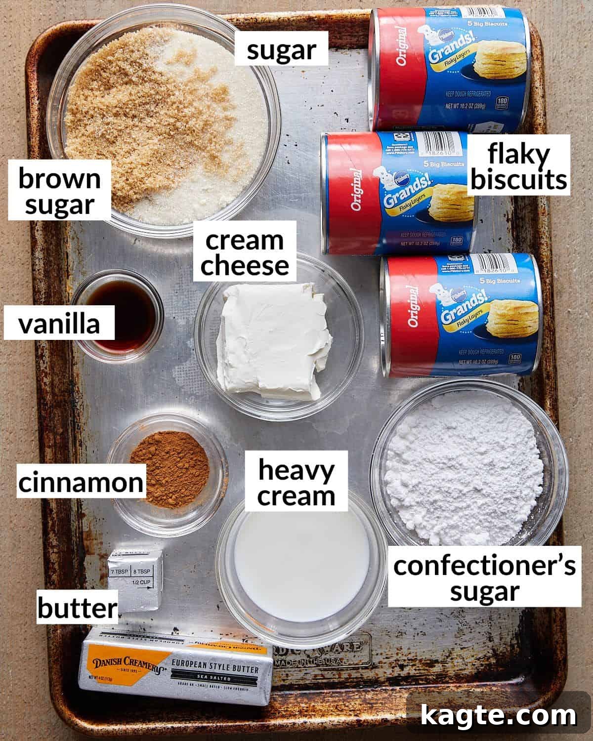 Overhead image displaying the simple ingredients needed for Dutch oven monkey bread: butter, sugars, cinnamon, canned biscuits, cream cheese, vanilla, and heavy cream.