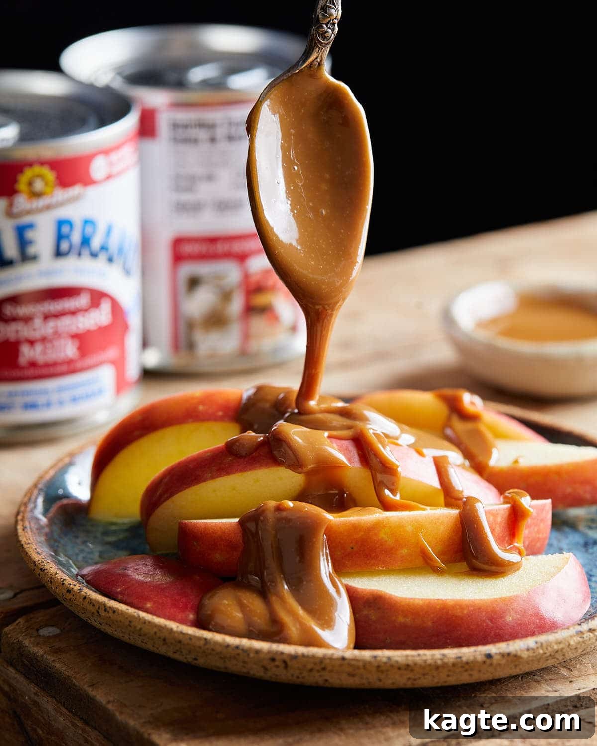 Close-up image of rich, amber-colored condensed milk caramel being generously drizzled over freshly sliced green apples, showcasing its perfect pouring consistency.