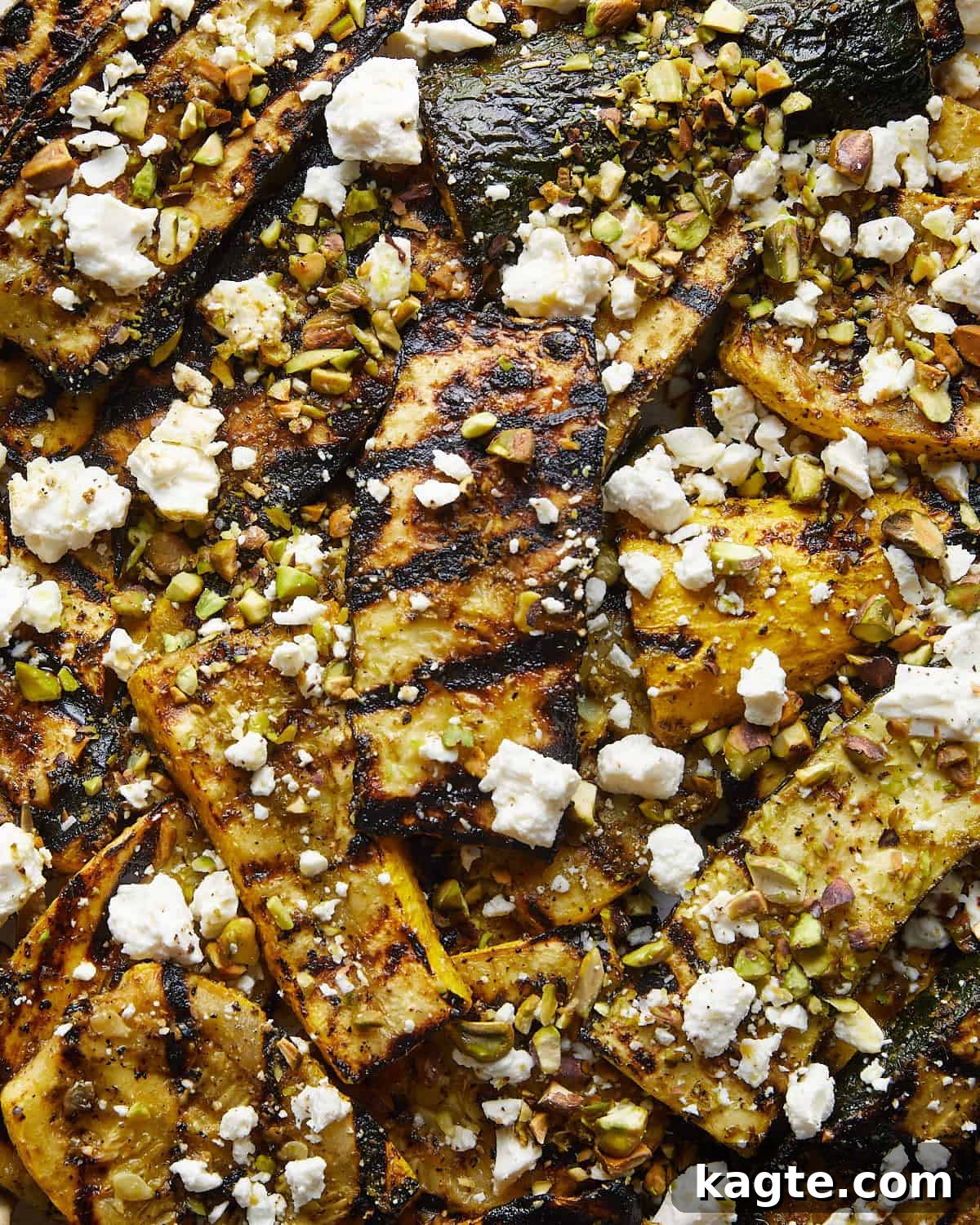 Summer's Grilled Squash Medley 5 Close-up image of vibrant grilled zucchini and yellow squash pieces glistening with pesto, topped generously with creamy feta cheese and crunchy pistachios, ready to be enjoyed.