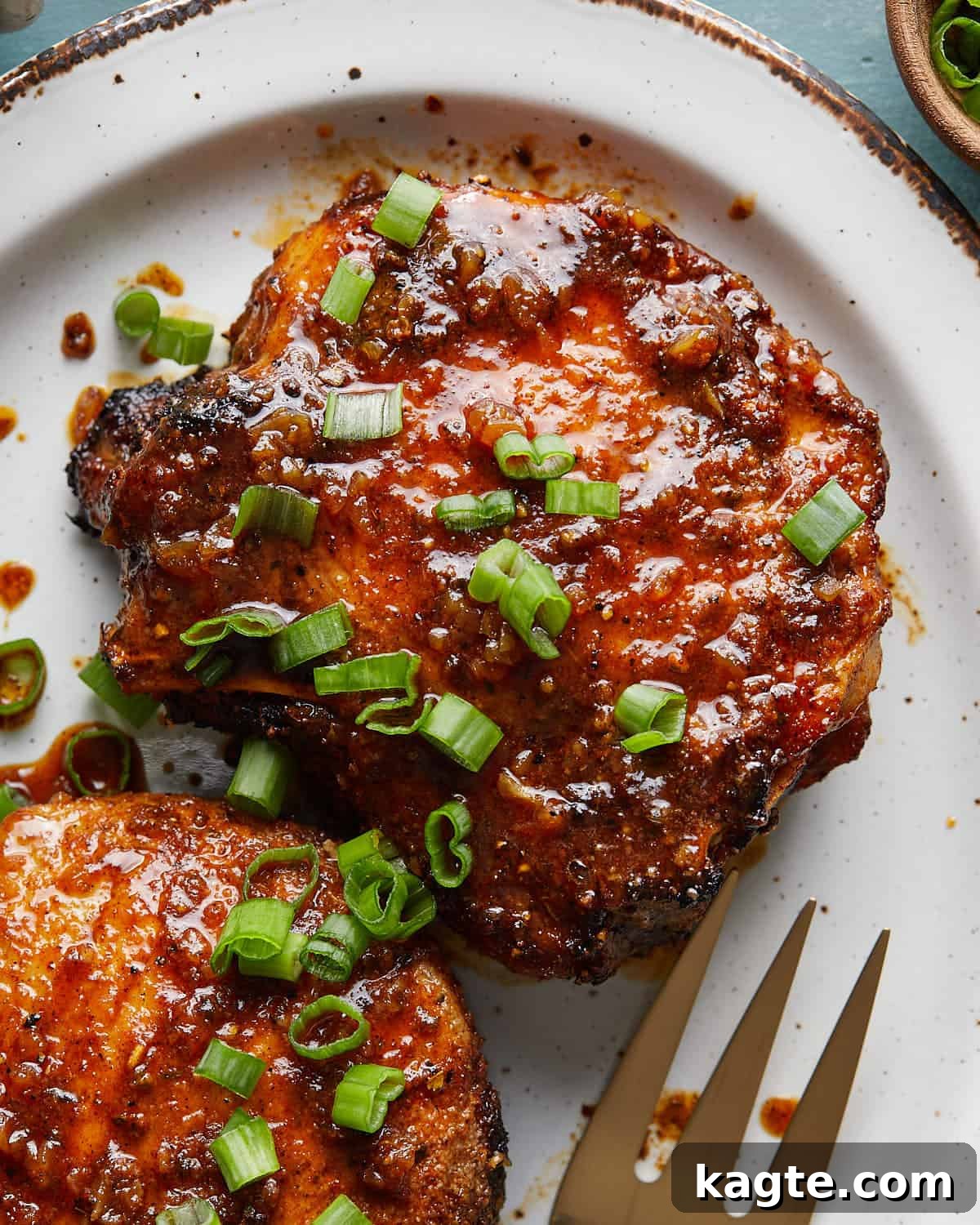 Close-up photo of a honey glazed pork chop on a plate, garnished with finely chopped green onions, highlighting the glistening glaze.