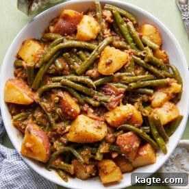 Close-up of a serving of green beans and potatoes, seasoned with herbs and bacon.