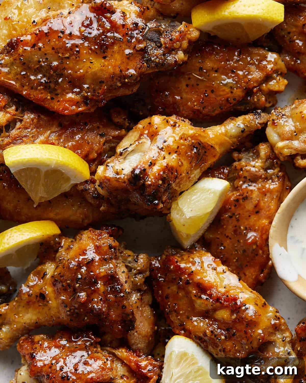 Honey Glazed Lemon Pepper Wings 5 Up close image of a stack of golden honey lemon pepper wings, glistening with sauce, garnished with lemon wedges, highlighting their crispy texture and sticky glaze.