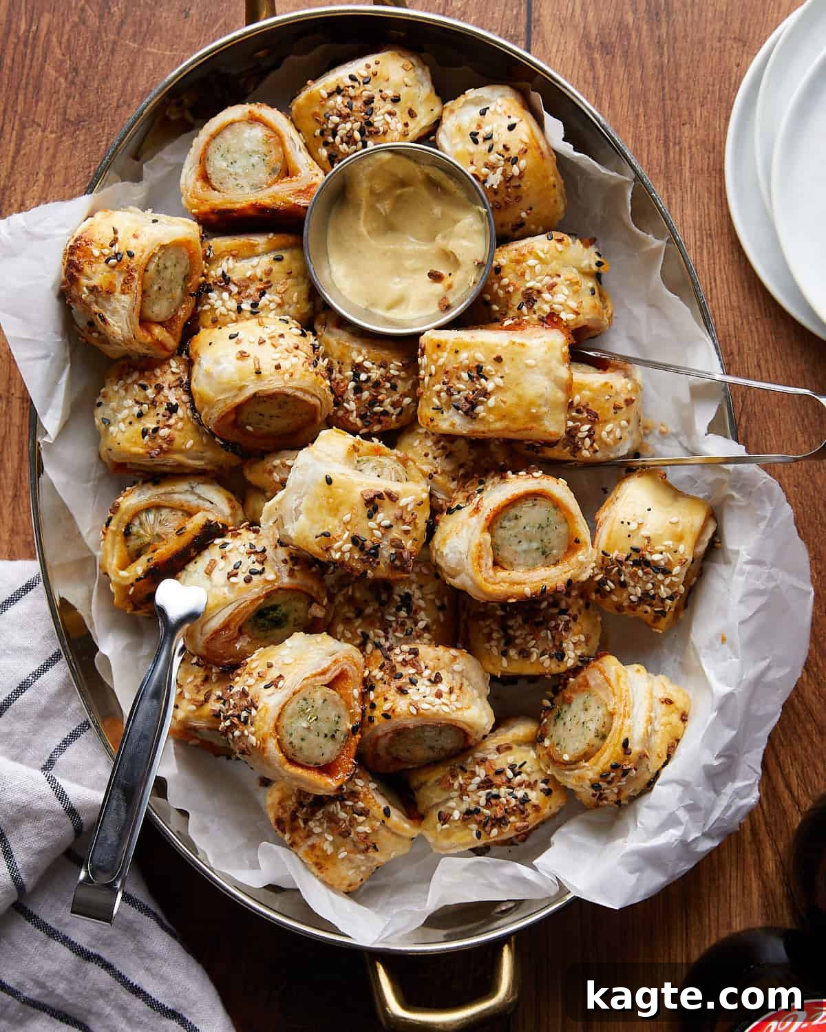 Flaky Golden Chicken Sausage Rolls 2 Overhead image of golden brown chicken sausage rolls arranged on a rustic metal plate, with a small dipping sauce bowl on the side, ready to be served as an appetizer.