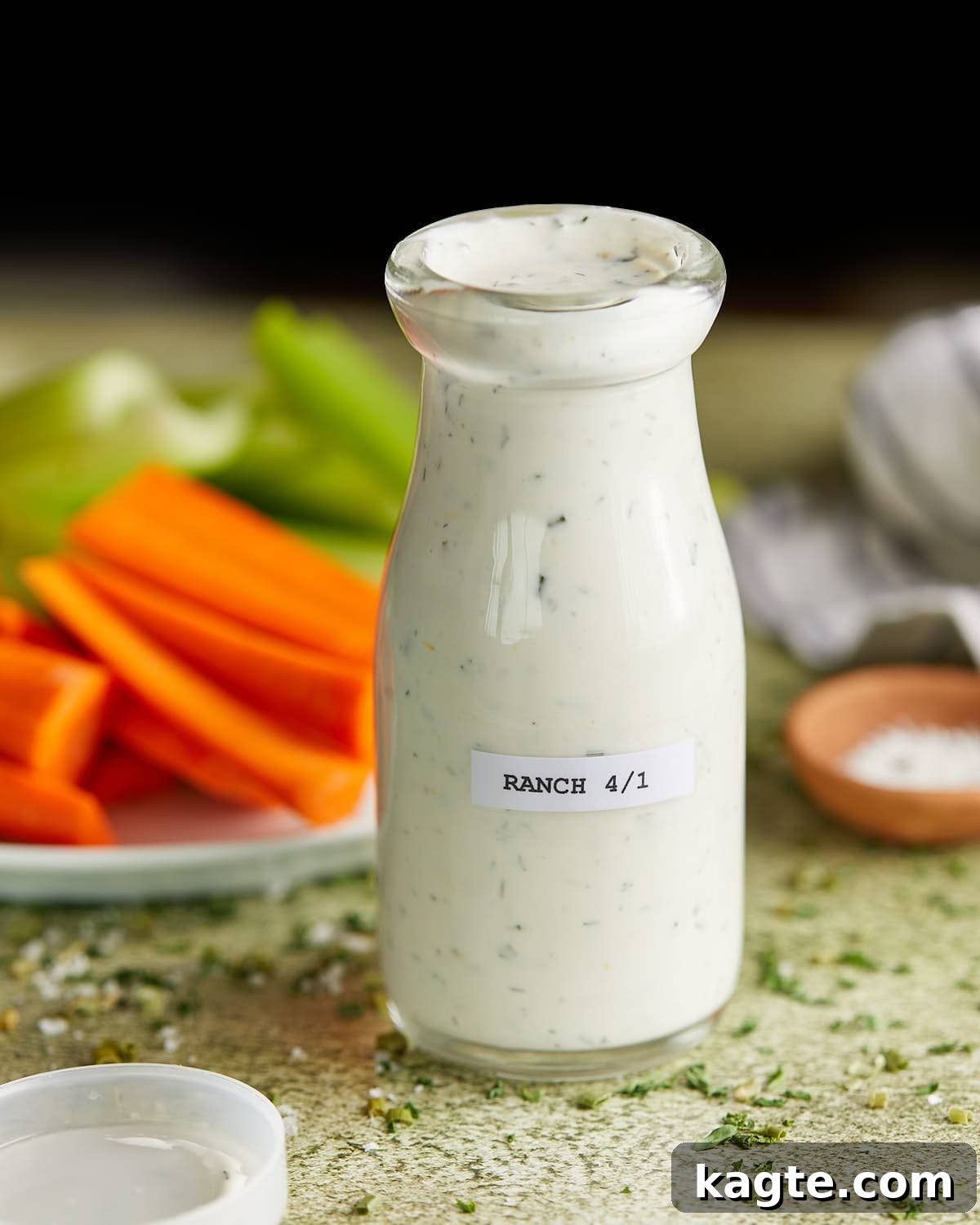 Tangy Greek Ranch Creation 2 Up close image of glass jar with homemade greek yogurt ranch dressing. Carrots and celery sticks in the background, ready for dipping.