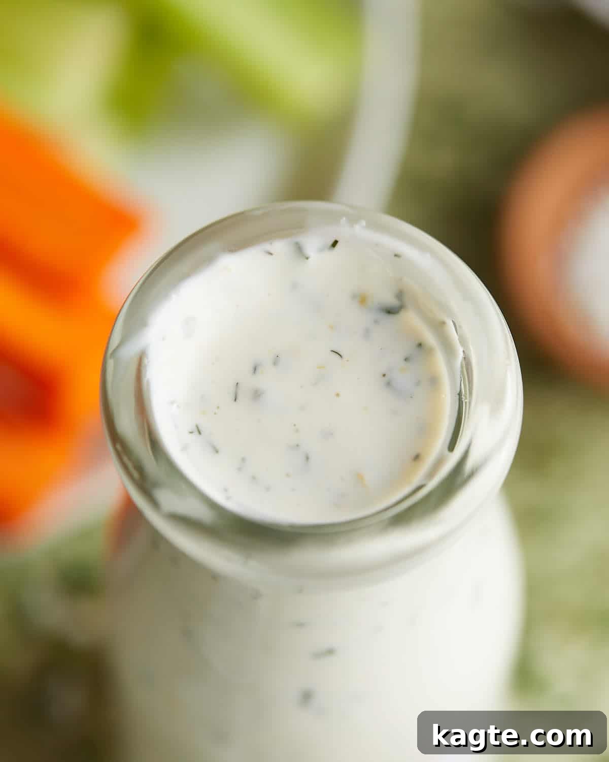 Tangy Greek Ranch Creation 5 Overhead image of homemade greek yogurt ranch dressing in a clear glass jar, garnished with fresh herbs.