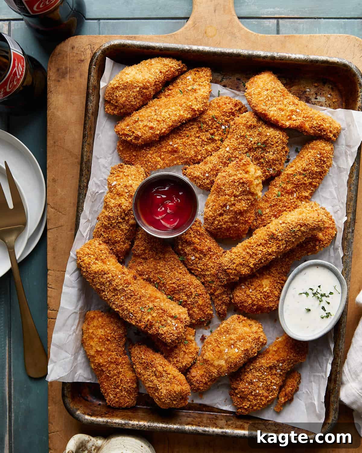 Overhead image of golden crispy chicken tenders served with ketchup and ranch dips on a parchment-lined baking sheet.