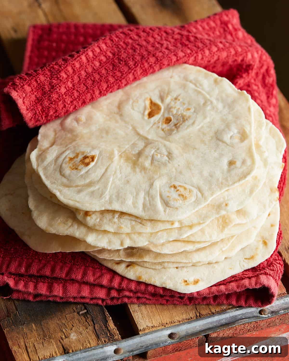 Up close image of homemade flour tortillas wrapped in red towel, showcasing their soft texture.