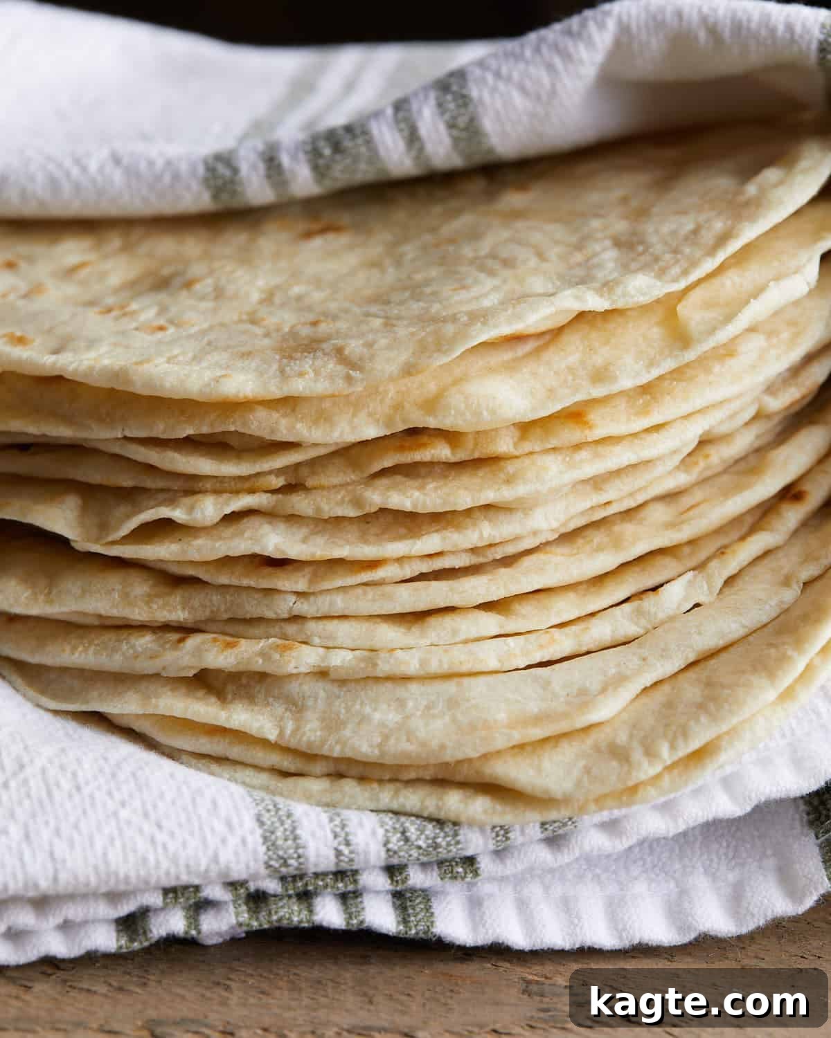 Up close side image of homemade flour tortillas wrapped around striped towel, ready to be served.
