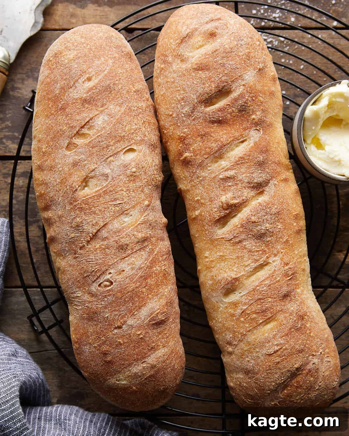 Perfectly Crusty Homemade French Bread 6 Overhead image of two loaves of French bread on wire rack with butter on the side.