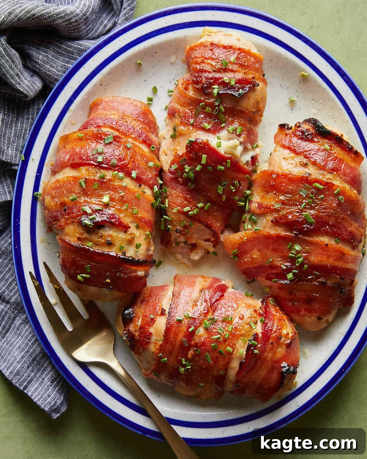 Crispy Bacon-Wrapped Stuffed Chicken Breast, Oven-Baked 5 Overhead image of bacon wrapped stuffed chicken breasts with garnish on white dish with fork.