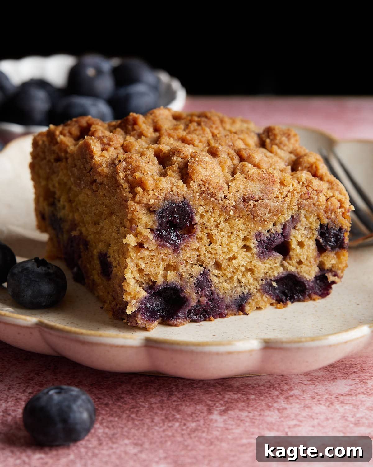 Tangy Greek Yogurt Blueberry Coffee Cake with Buttery Streusel 2 Close-up side profile of a delicious slice of blueberry coffee cake on a white plate, showcasing the crumbly streusel topping and plump blueberries.