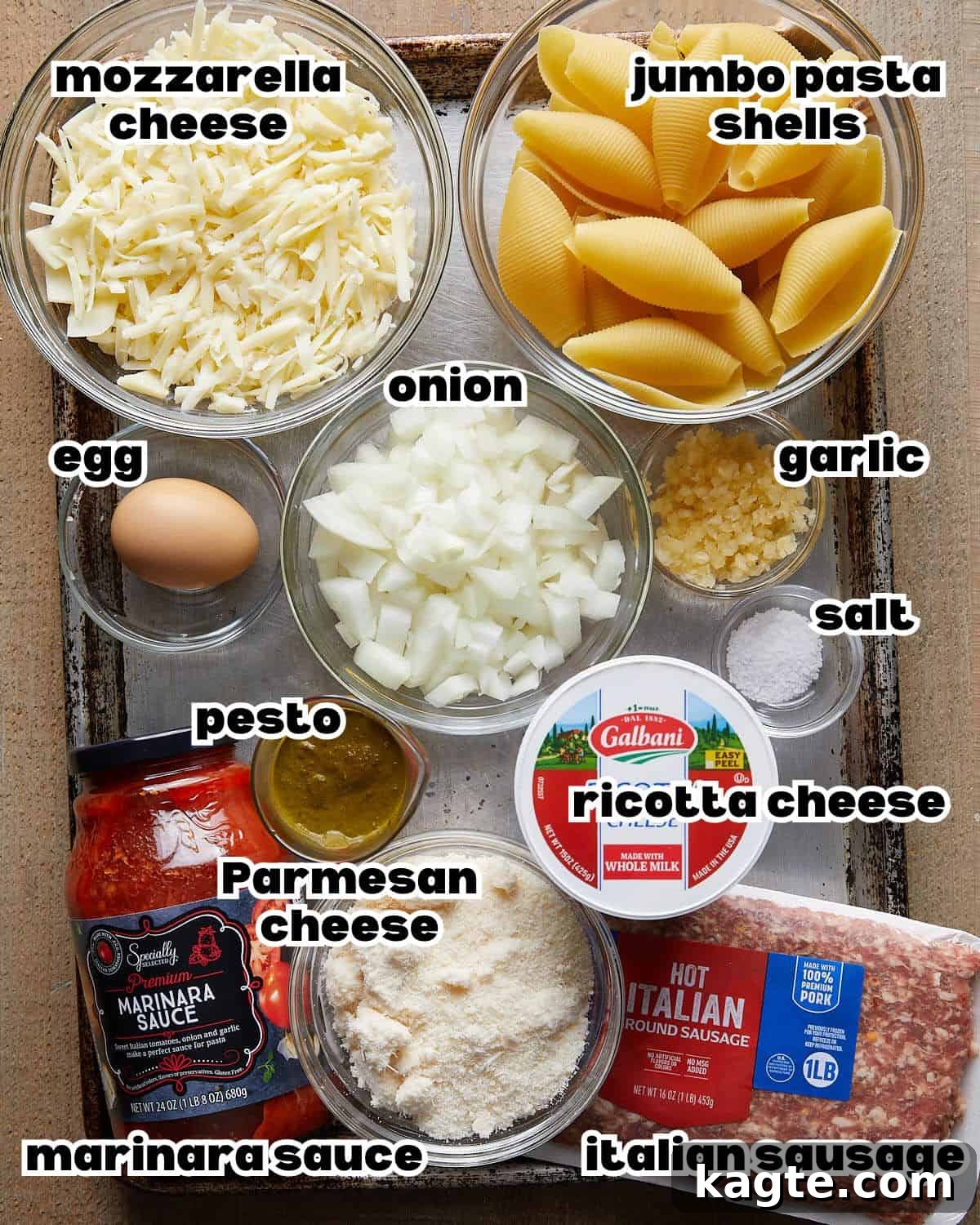 Ingredients needed to make baked stuffed shells, including jumbo pasta shells, ricotta cheese, mozzarella, marinara sauce, eggs, garlic, and pesto.