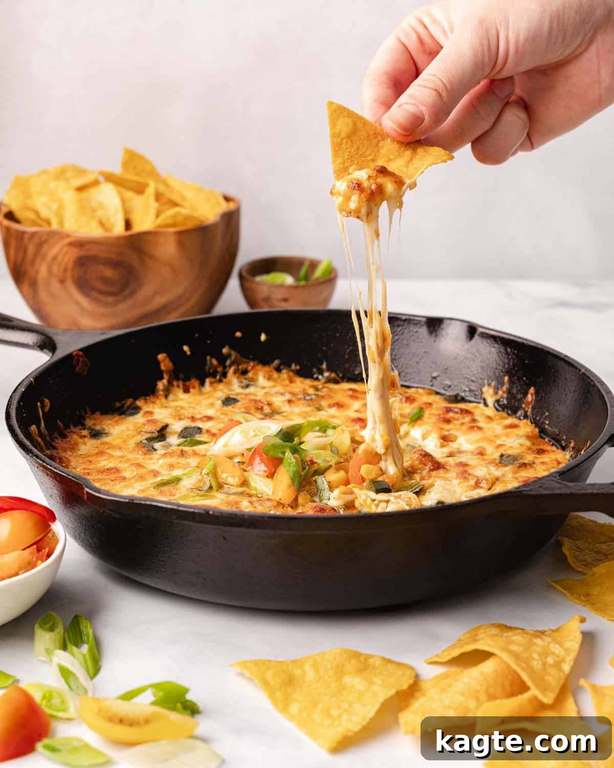Melty Fiesta: Poblano-Corn Fundido 2 Crispy tortilla chip dipping into a bubbling, golden-brown Queso Fundido with visible corn and poblano pieces.