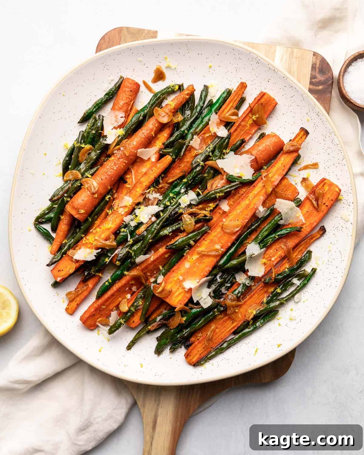 Golden Roasted Green Beans and Carrots 2 Roasted green beans and carrots on a white plate, garnished with lemon zest and parmesan.