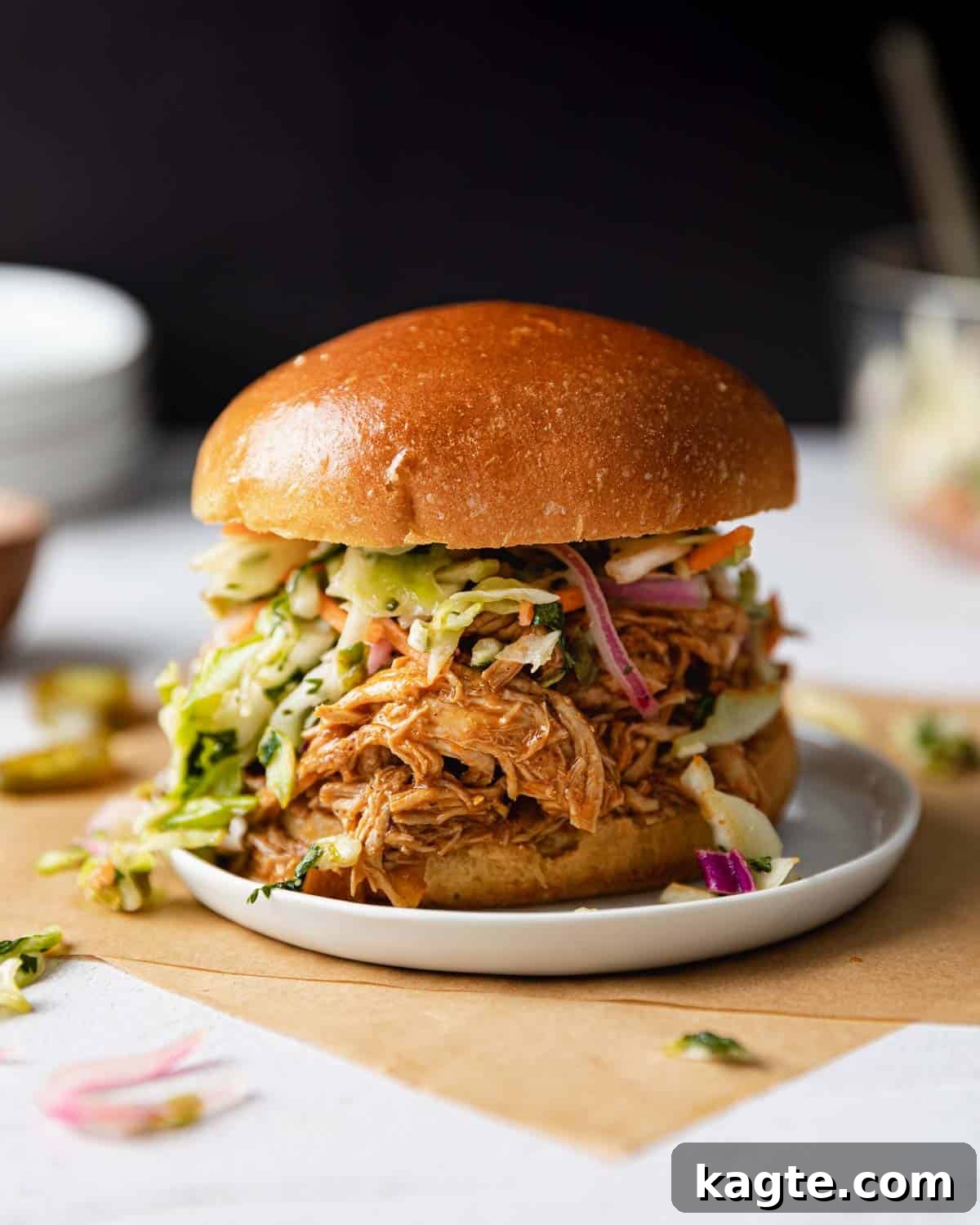 Close-up image of a delicious Instant Pot BBQ chicken sandwich on a white plate, showcasing the shredded chicken and sauce.