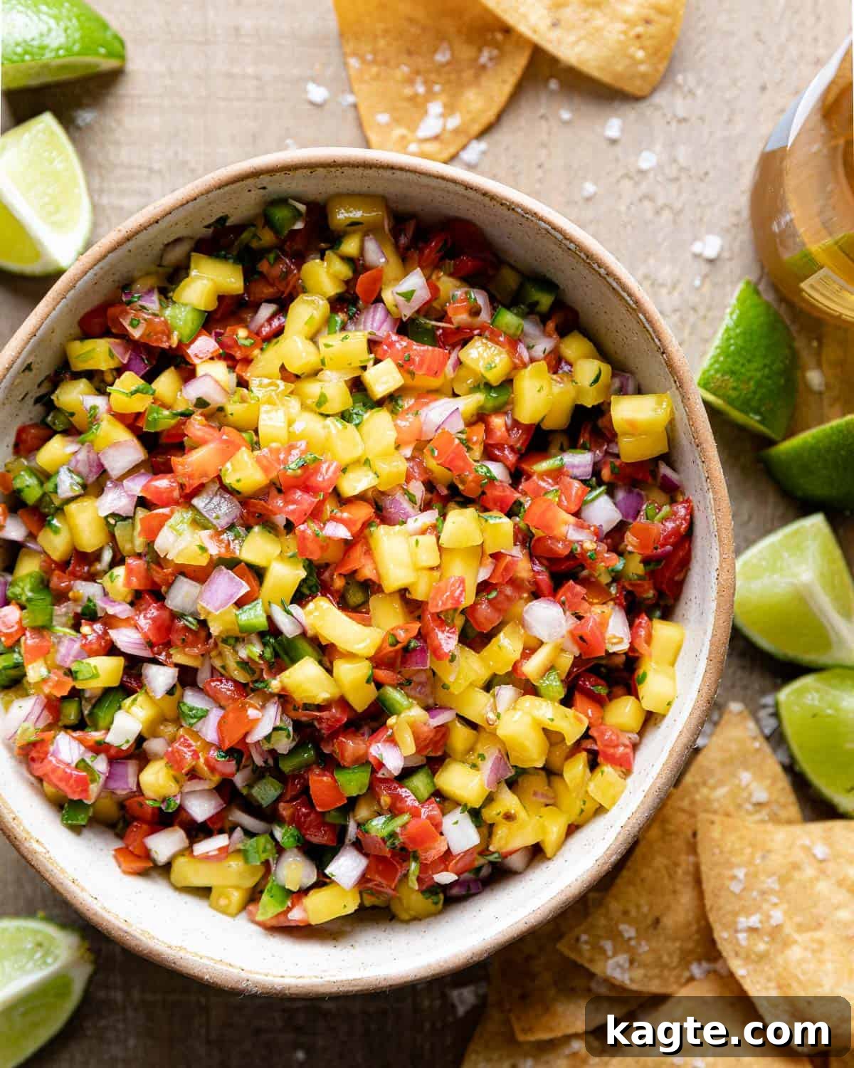 A beautifully arranged overhead shot of vibrant Mango Pico de Gallo in a white bowl, garnished with fresh cilantro, ready to be served. The bright colors of mango, tomatoes, and red onion are prominently featured, evoking a fresh and summery feel.