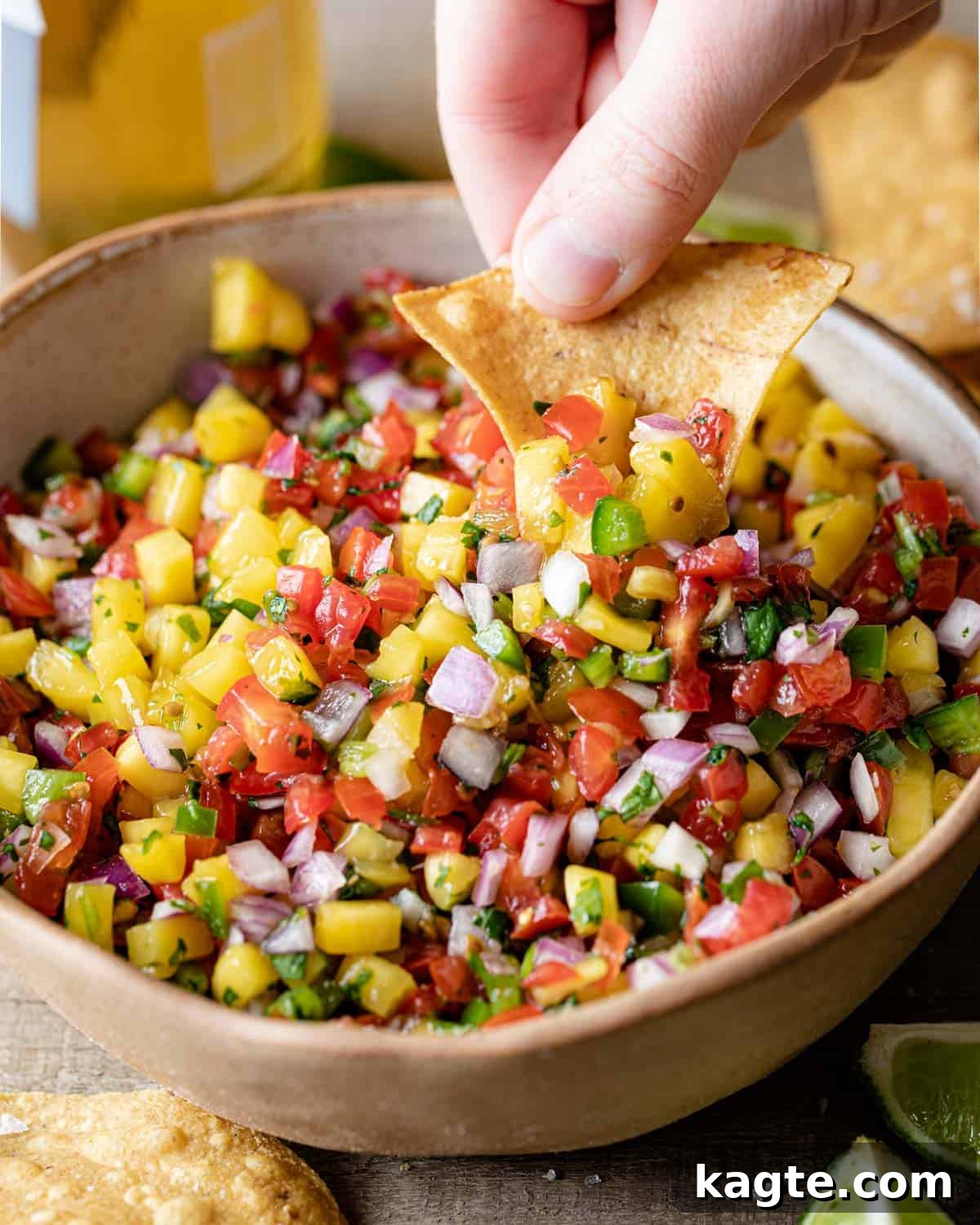 A close-up shot of a tortilla chip being dipped into a bowl of colorful Mango Pico de Gallo, highlighting the fresh ingredients and inviting texture.