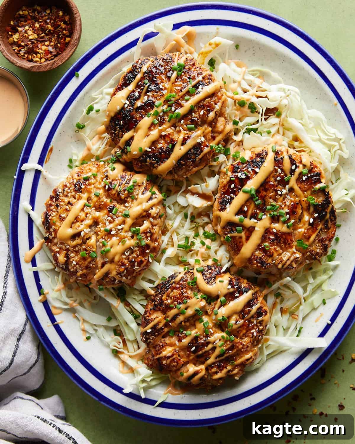 Flavor-Packed Salmon Burgers with Zesty Sriracha Aioli 9 Overhead shot of juicy Asian salmon burgers served as patties over a fresh shredded cabbage bed, topped with herbs and sesame seeds