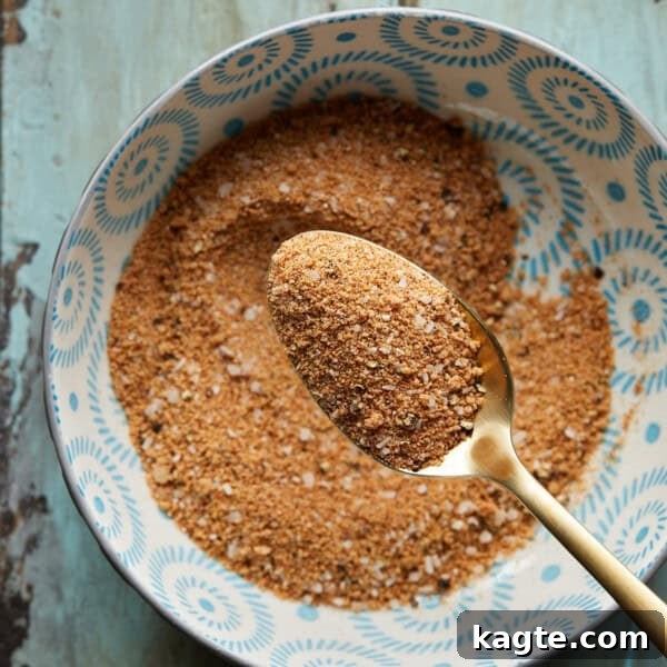 Juicy Grilled Hamburger Recipe for Perfect Backyard Burgers 9 Overhead photo of a bowl of burger seasoning with a gold metal spoon on a rustic surface.