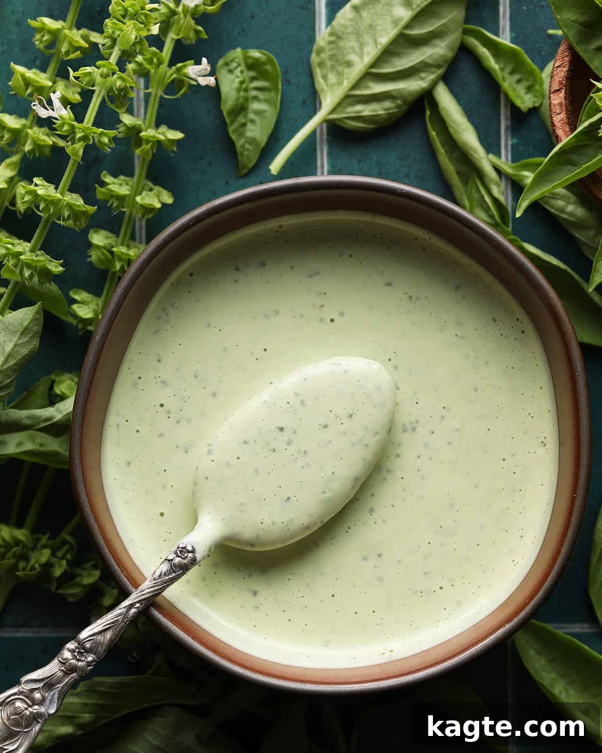 Creamy Homemade Basil Aioli 5 Bowl of creamy basil aioli with a spoon and fresh basil in the background.