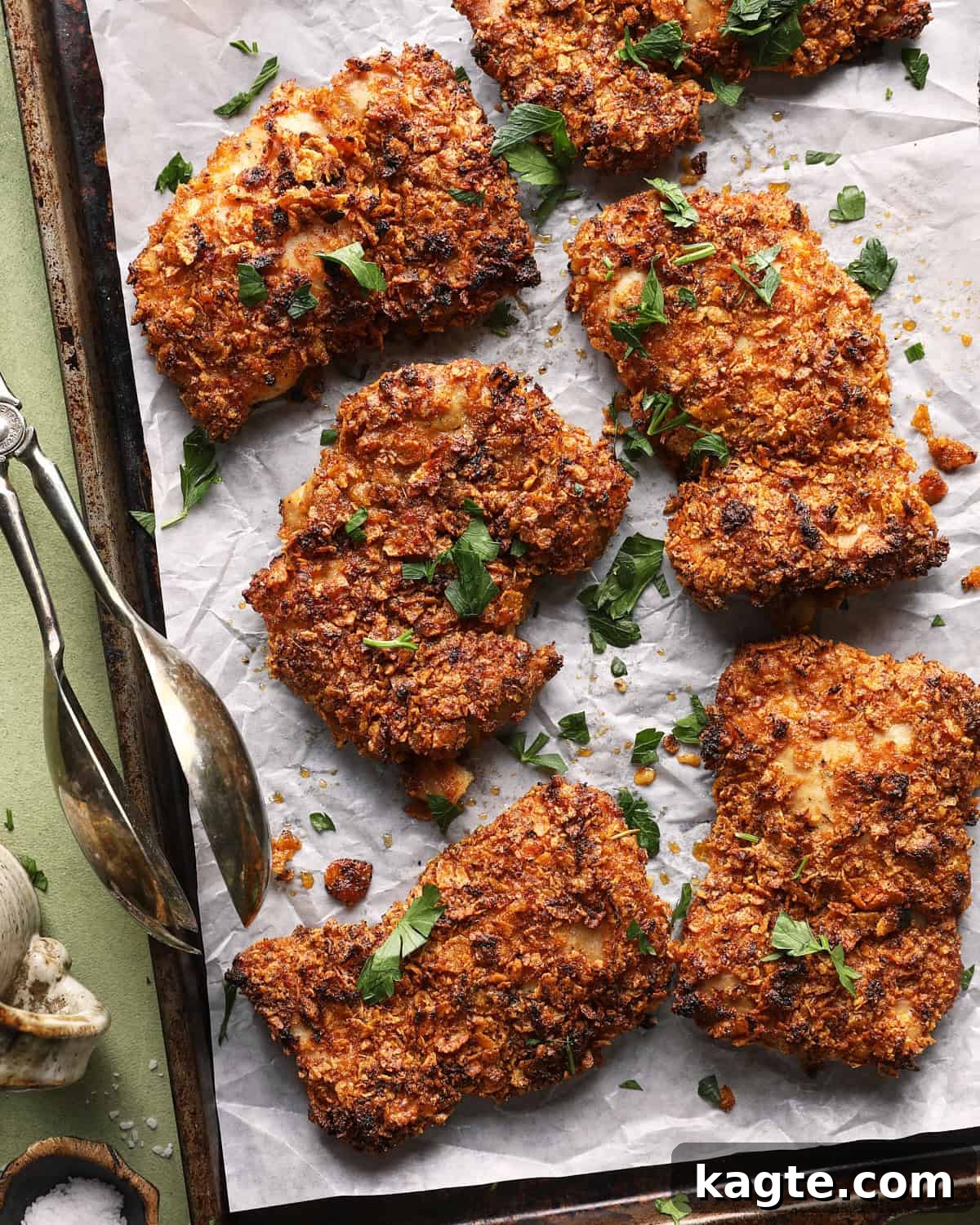 Crispy Baked Cornflake-Crusted Chicken Thighs 2 Crispy baked cornflake chicken thighs garnished with chopped parsley on a parchment-lined sheet pan.