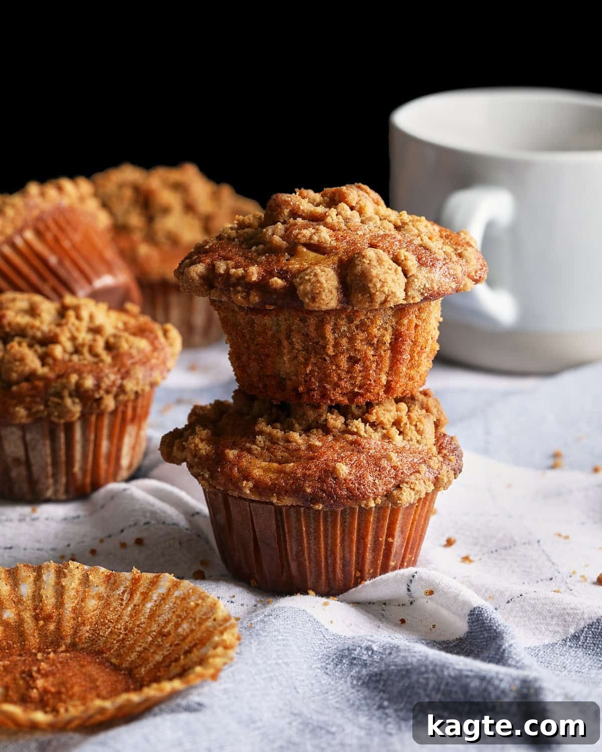 Apple Cider Muffins with Cinnamon Crumb Topping 2 Apple cider muffins stacked 2 high with apple cider in a mug in the background