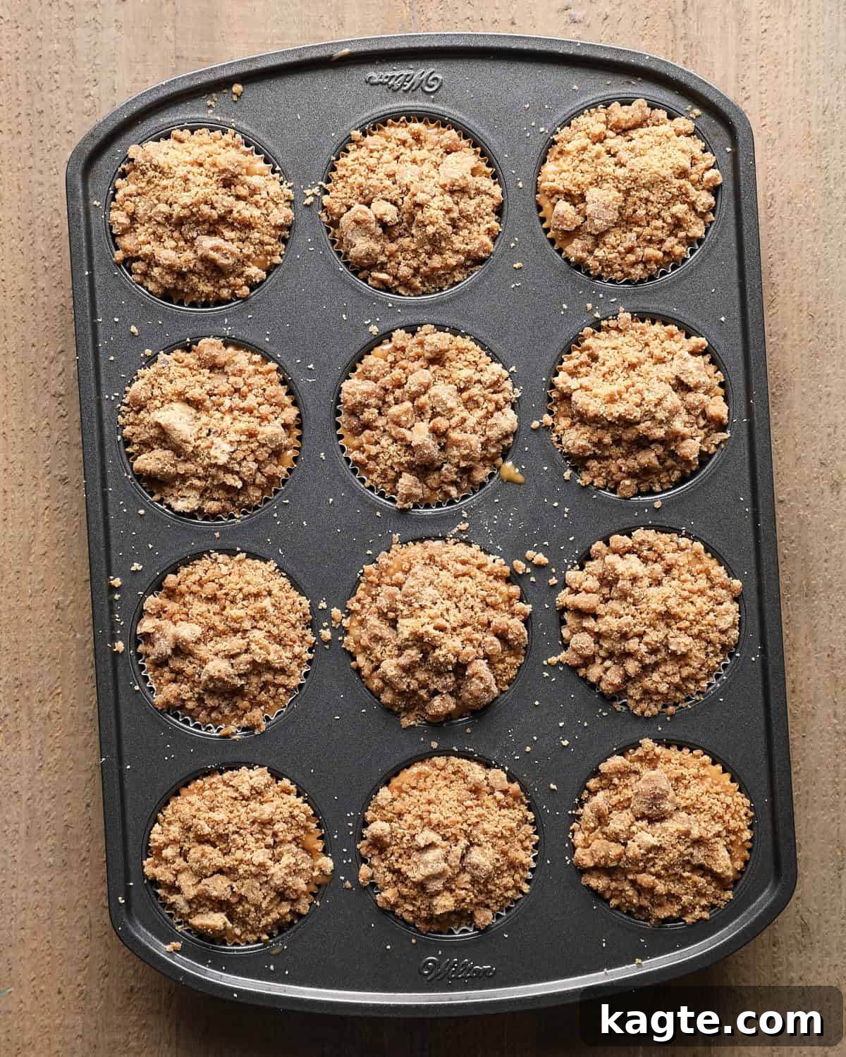 Apple Cider Muffins with Cinnamon Crumb Topping 7 Twelve lined muffin wells filled with batter and topped with cinnamon crumb before baking.