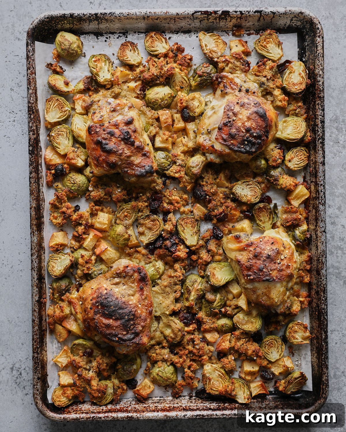 Sheet Pan Roasted Chicken with Herb Stuffing 7 Browned chicken thighs over roasted stuffing, Brussels sprouts, apples, and cranberries on a parchment-lined sheet pan.